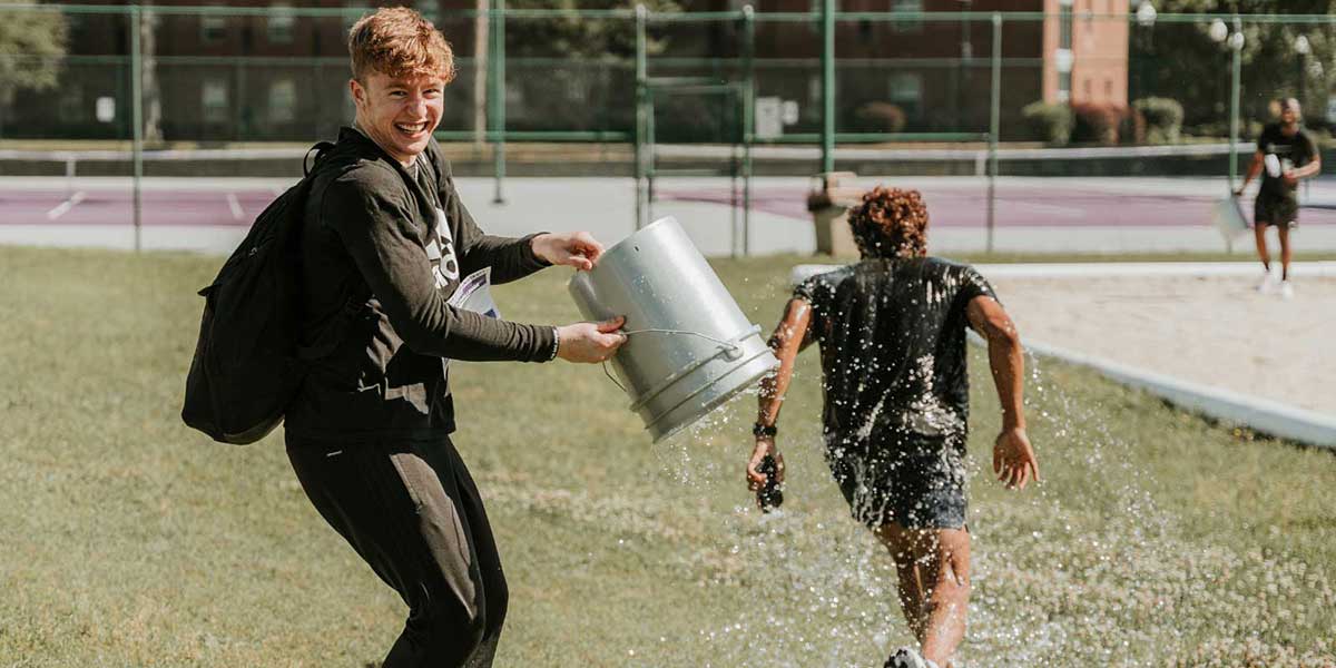 A student mischievously looks at the camera after splashing a bucket of water on his fellow teammate during the MGA Student Leadership event